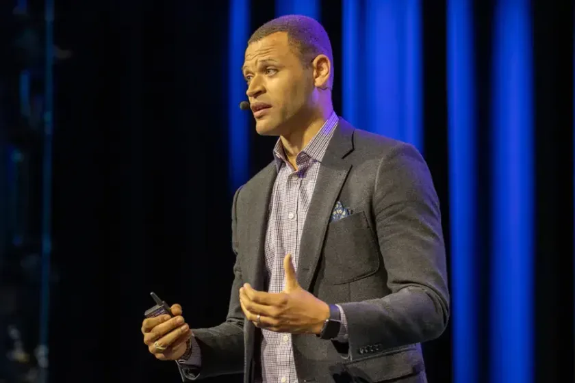 A speaker mid-gesture against a blue-lit curtain, 2019