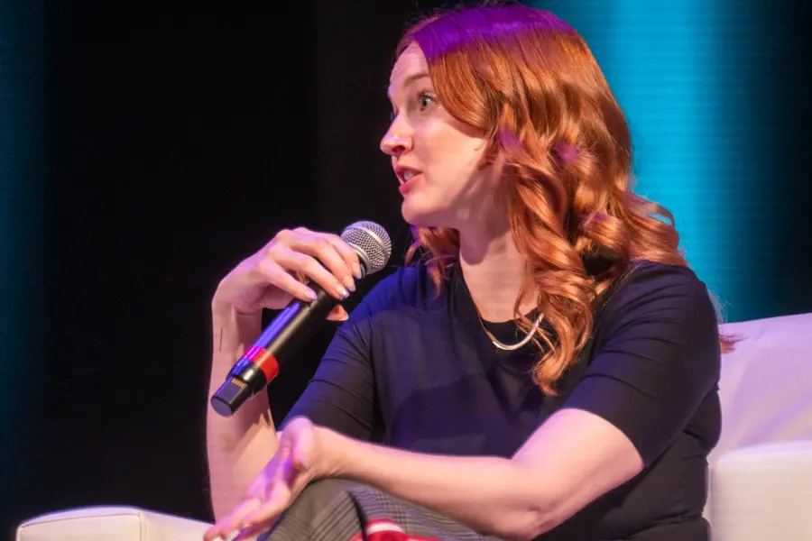 Dara Denney on a couch with a microphone during a panel, 2022